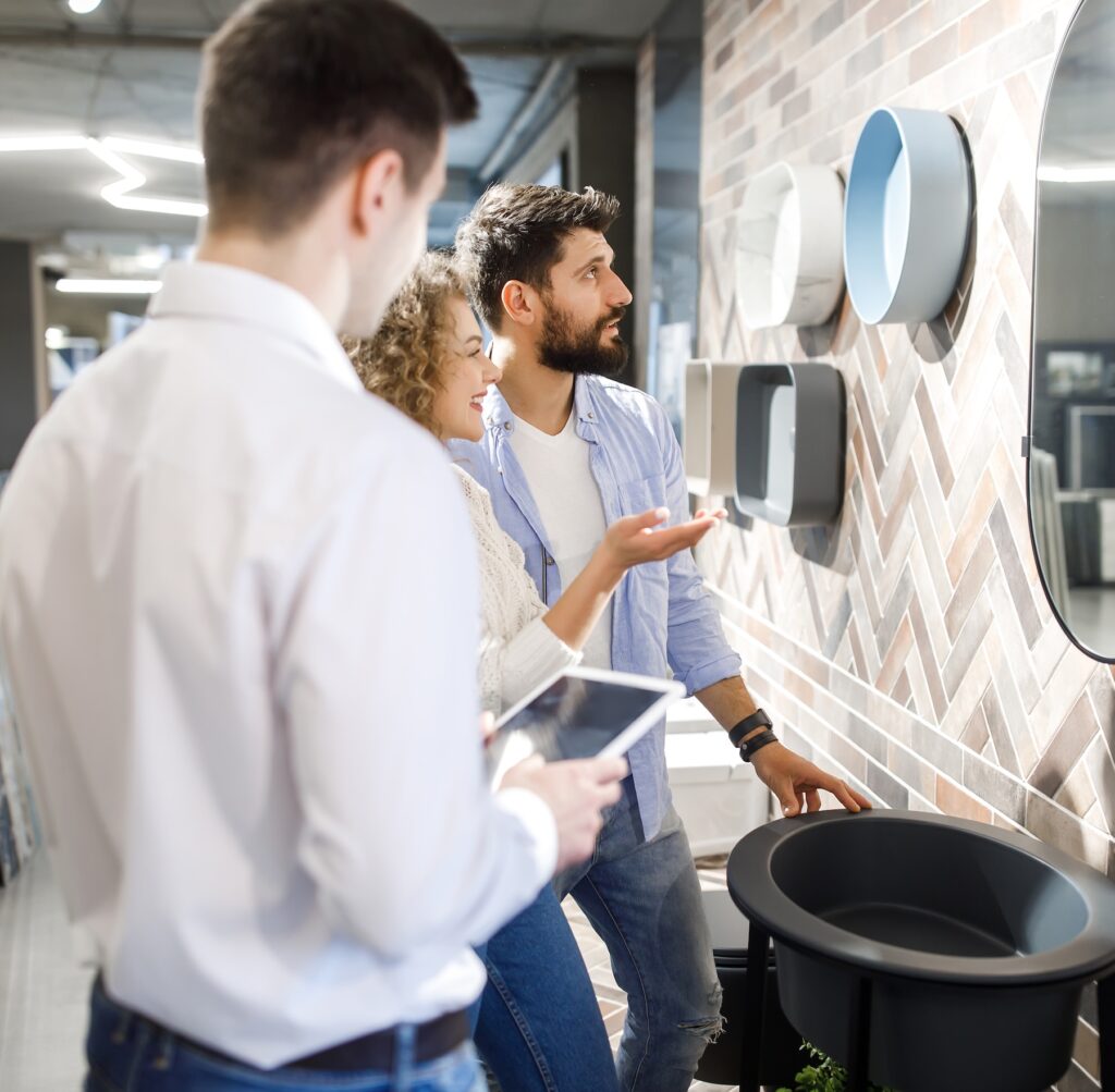 A husband and wife couple stand with a salesperson while choosing tile.