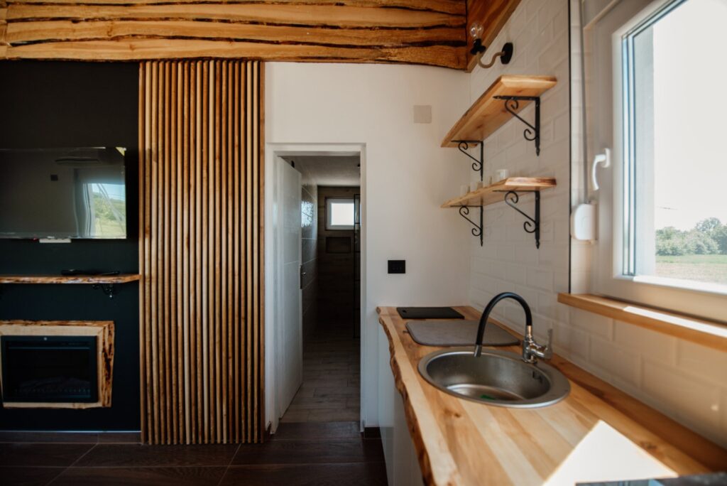A small kitchen with a thick butcher block countertop, a stainless sink, and open wooden shelves on iron brackets