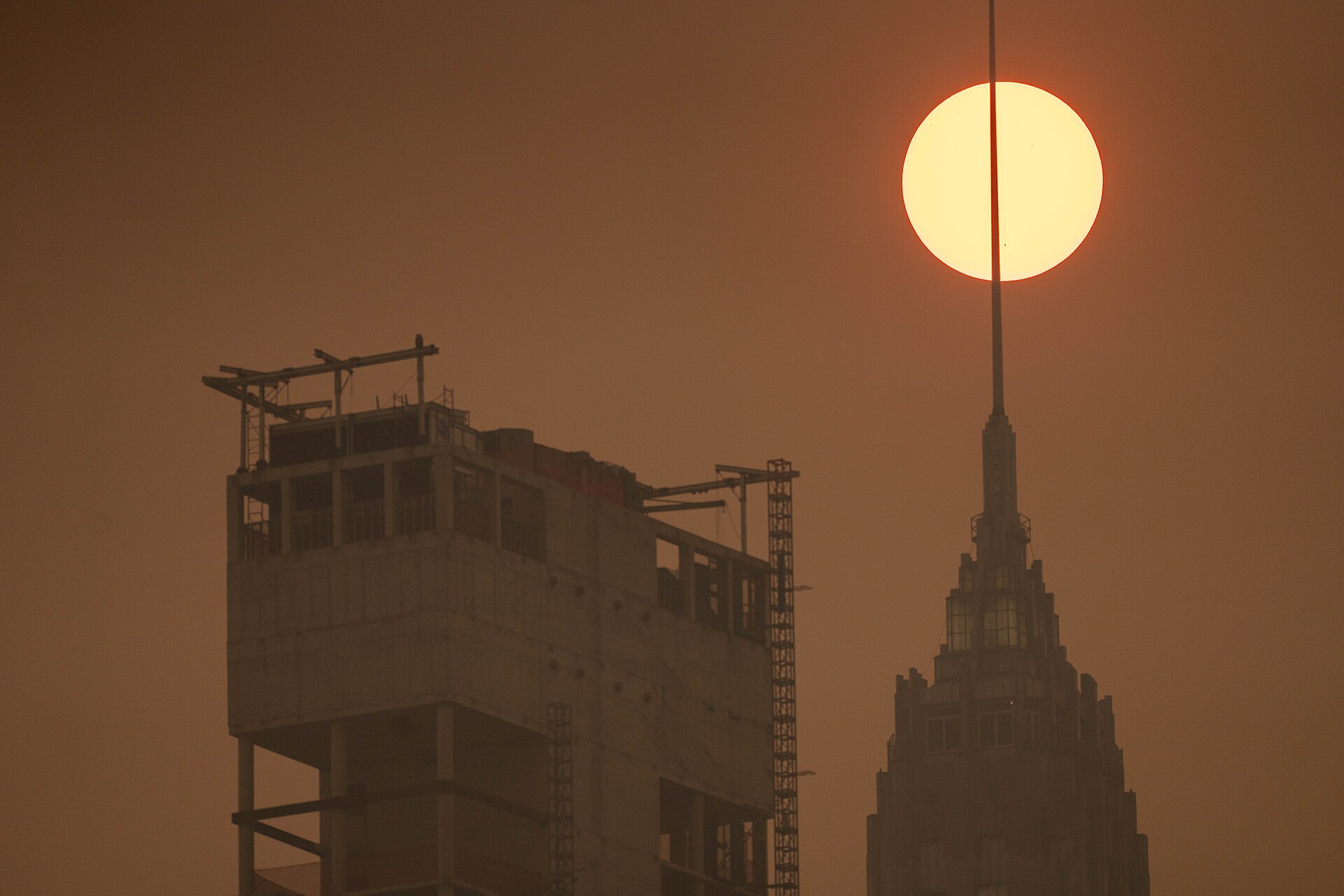 The sun glows as a dim orange disk through thick wildfire smoke above the Manhattan skyline