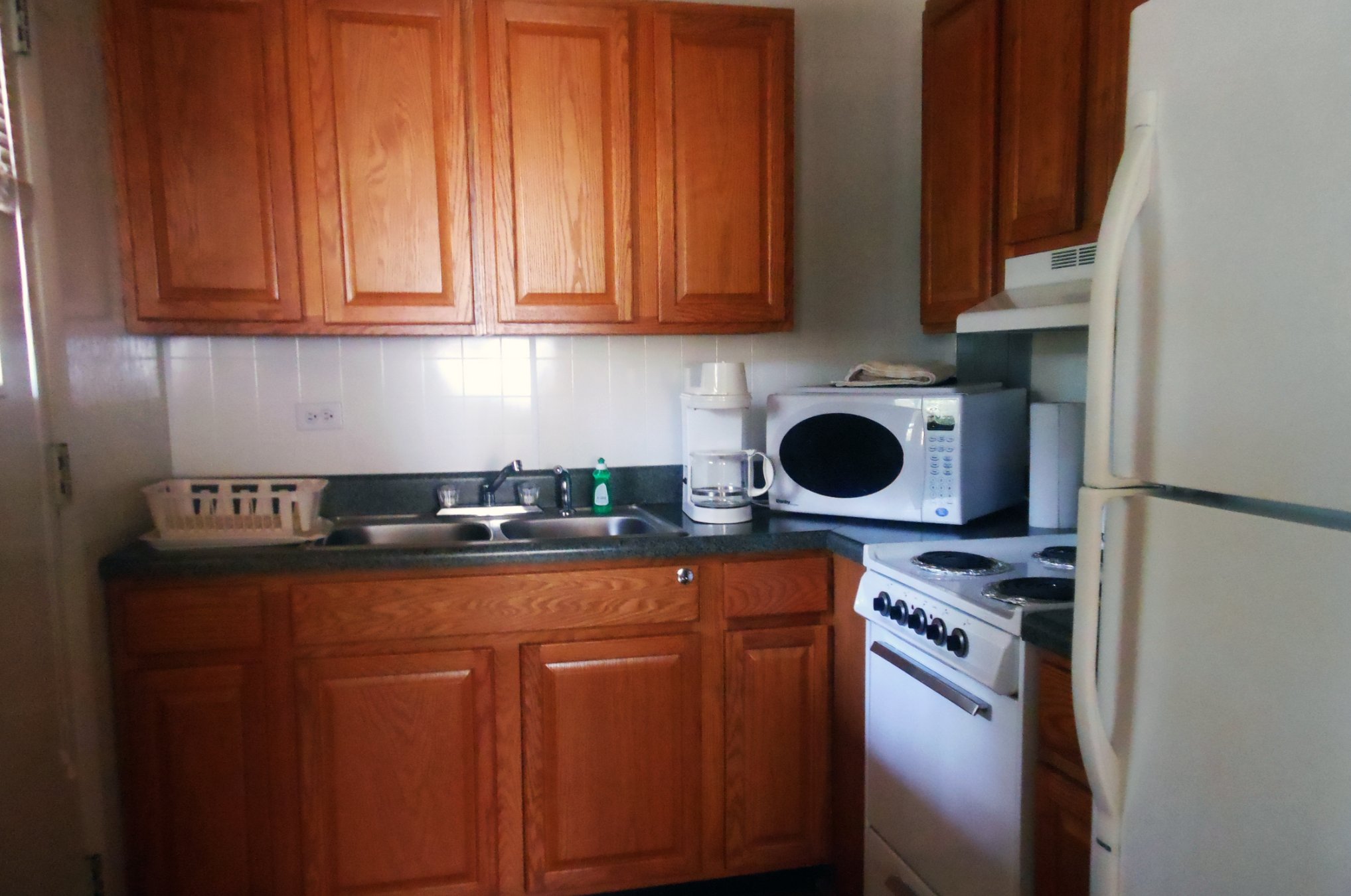 A kitchen lined with warm reddish-brown solid wood cabinets, white appliances, and a dark countertop