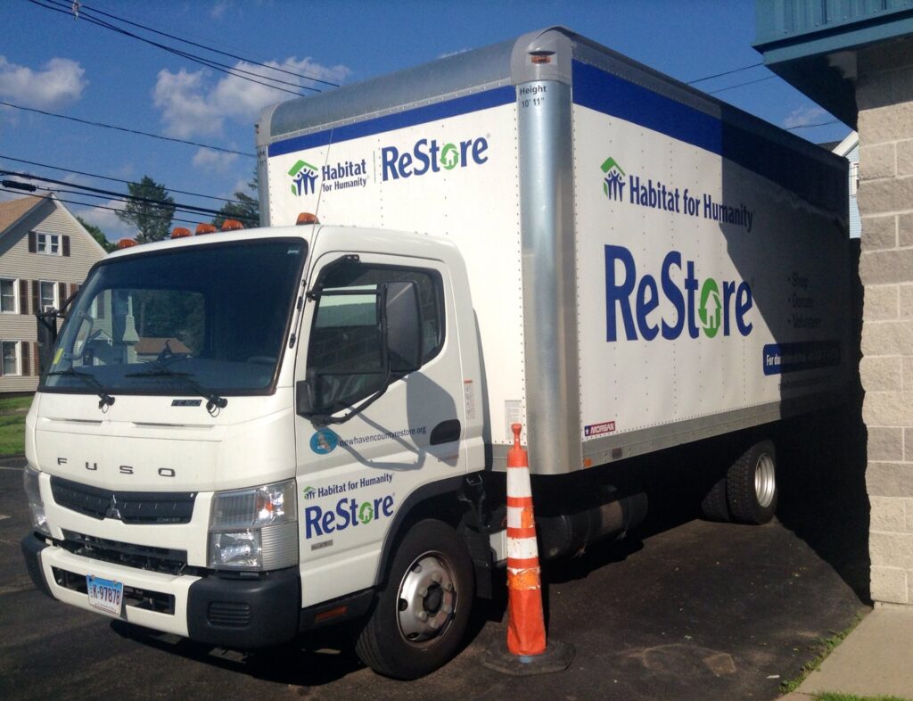 A white Habitat for Humanity ReStore box truck parked outside a store