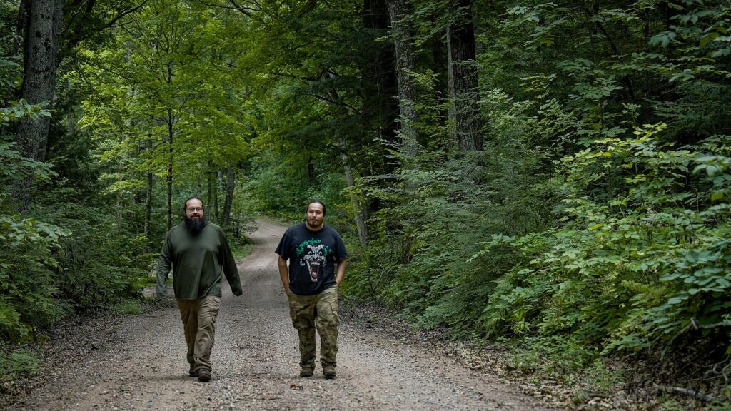 Two Menominee forestry workers walk a narrow dirt road through dense green forest